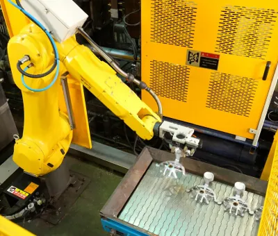 Automated Fanuc robotic arm extracting a fresh aluminum die cast component from a high-pressure casting machine to ensure cycle time consistency.