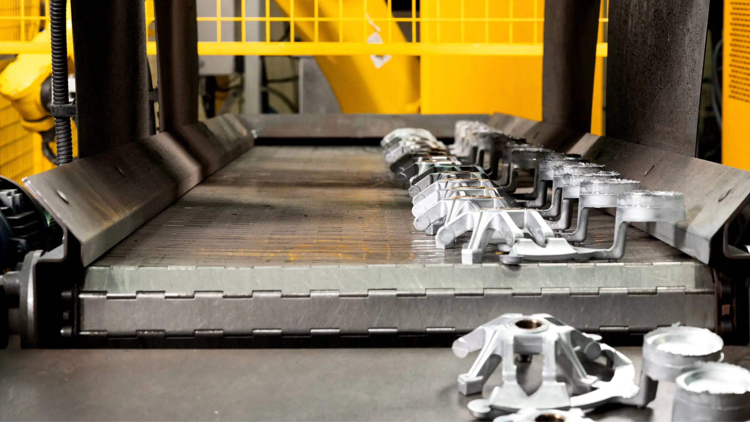 Freshly cast aluminum components on an automated conveyor system after high-pressure die casting and robotic trimming.